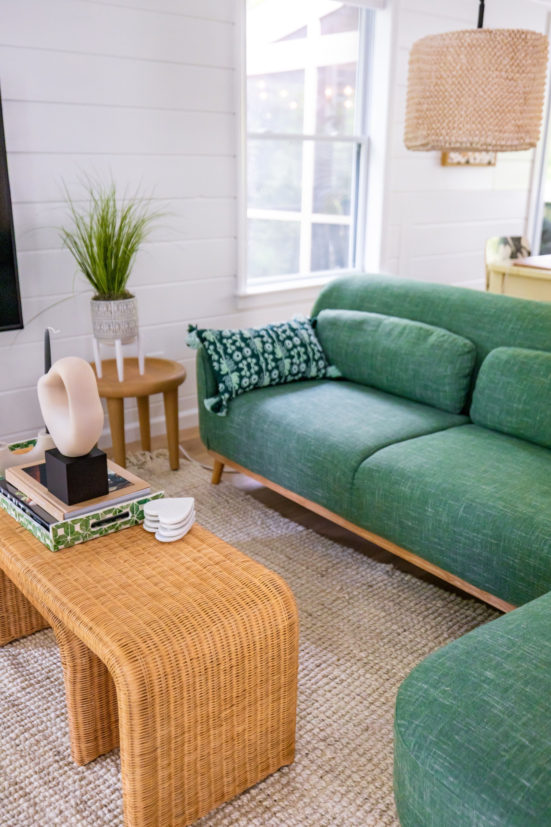 A sunlit living room with a green sofa and woven table, lifestyle photography